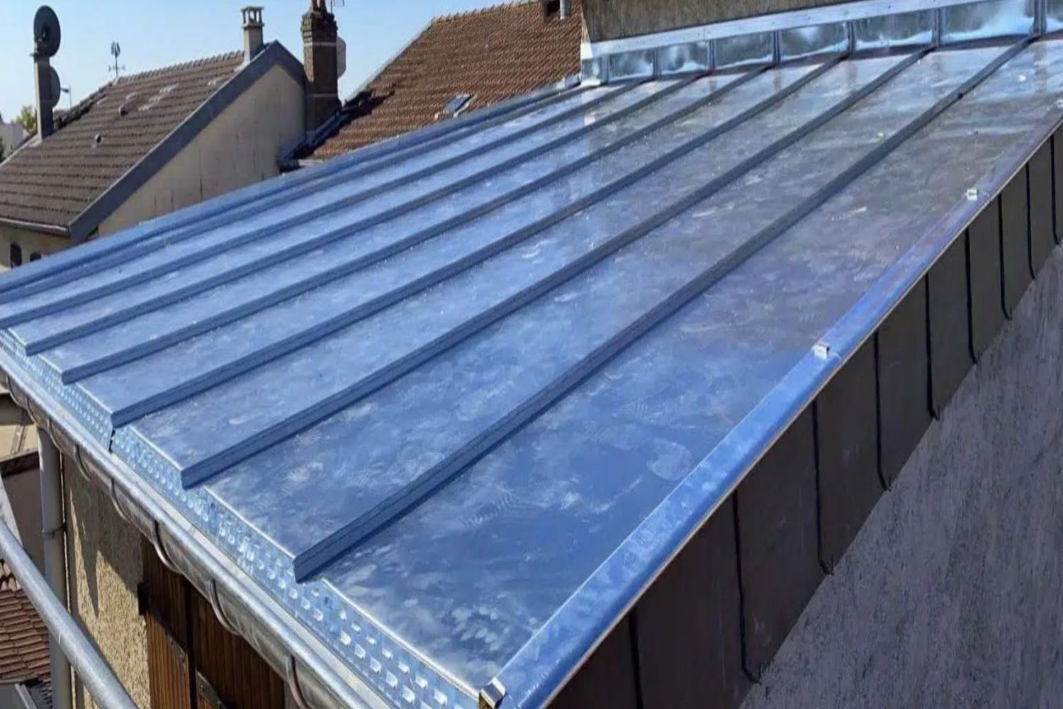 Toiture avec panneaux solaires bleus et claboussis d'eau, maisons avec cheminées en arrière-plan sous ciel dégagé