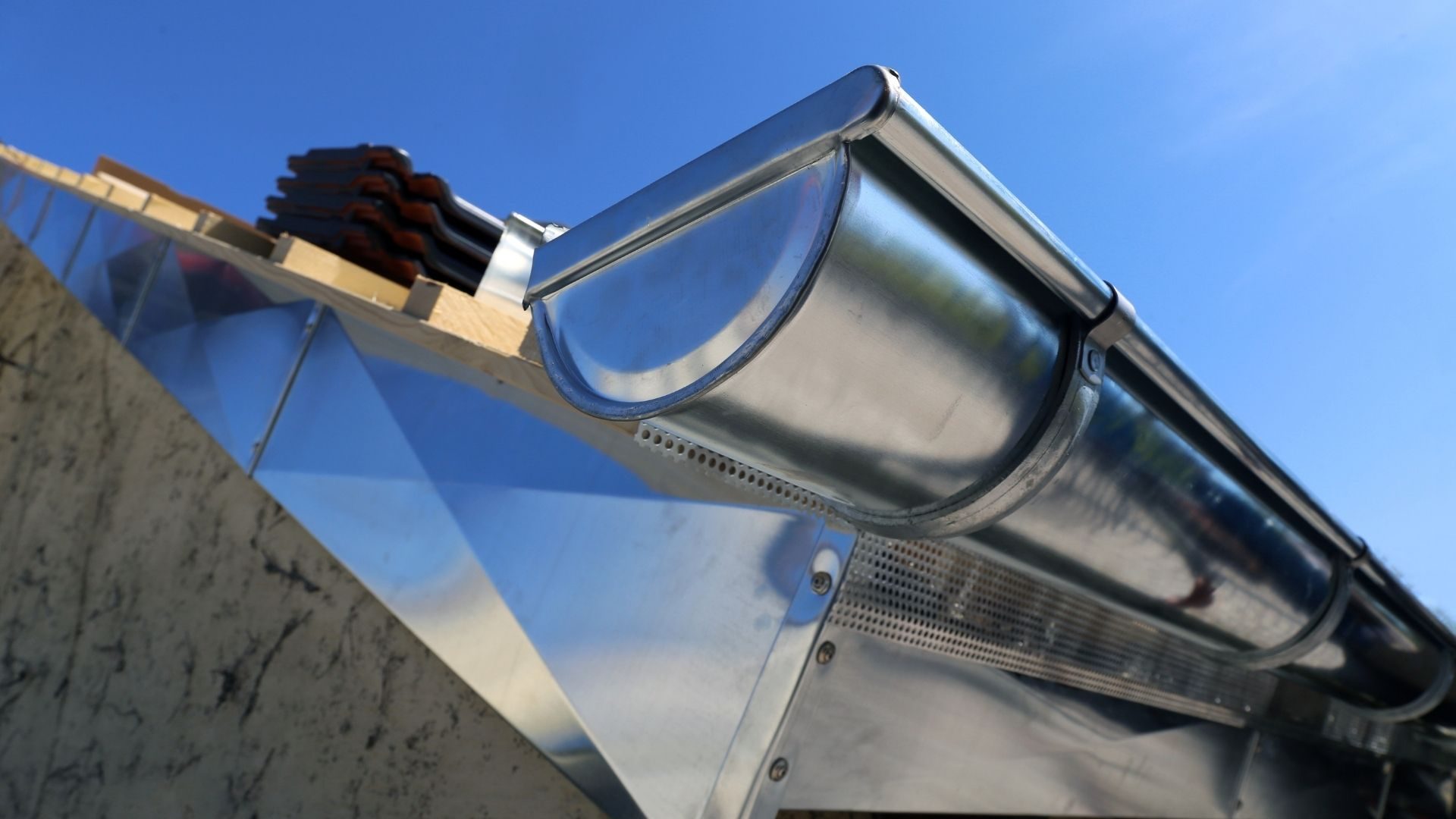 Gouttière métallique grise avec support de fixation et tuyau de descente installée sur façade en pierre